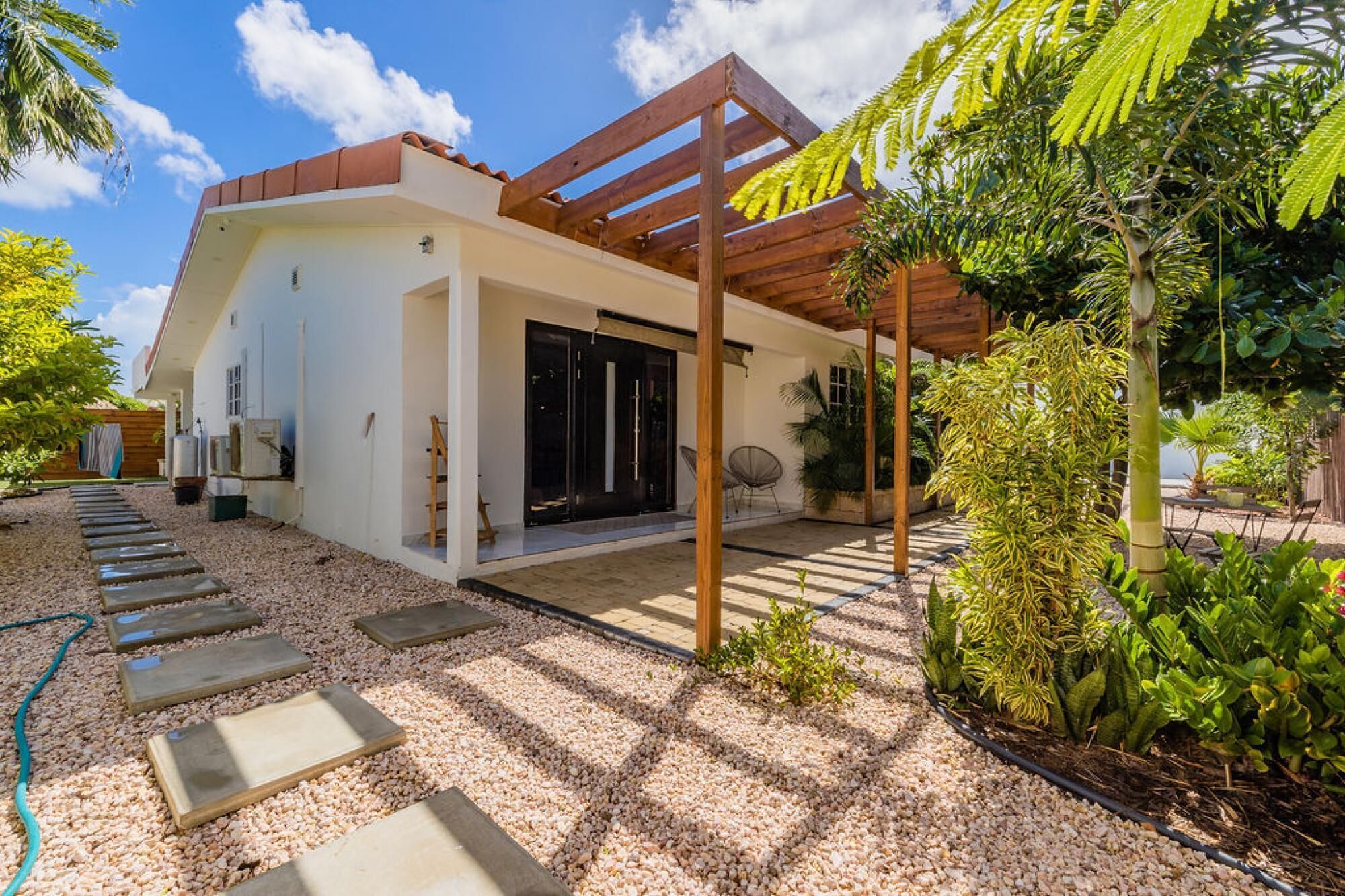 Una casa moderna con un porche cubierto, un sendero de grava y abundante vegetación.