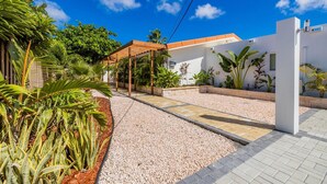 A residential property with a paved driveway, a wooden pergola, and a variety of tropical plants. - NEW 4br3ba Villa Near Eagle Beach w Private Pool (Oranjestad)