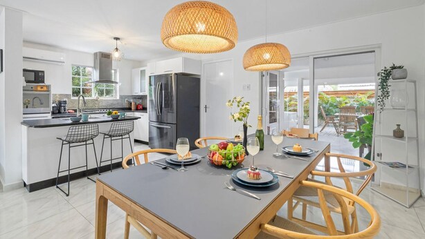 A modern kitchen with a dining area, featuring a large island, stainless steel appliances, and wicker pendant lights. - NEW 4br3ba Villa Near Eagle Beach w Private Pool (Oranjestad)