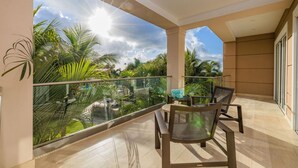 Un balcon doté d’une balustrade en verre, une table avec des chaises et une vue sur des palmiers et une piscine.
