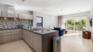 Une cuisine moderne avec un îlot central, un coin repas doté d’un canapé bleu et un balcon aménagé avec du mobilier d’extérieur.