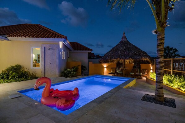 Relax by the pool, surrounded by lush landscaping and a thatched-roof building.
