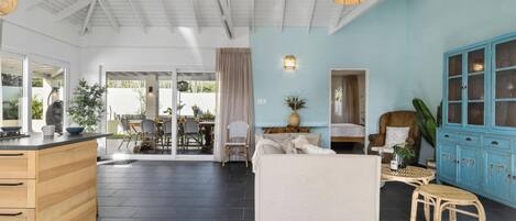 Een ruime woonkamer met een grote witte bank, een eettafel met stoelen, een keuken met een houten kast, en een blauwe kast met glazen deuren.