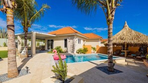 A pool area with a house, palm trees, and a thatched structure. - NEW Villa - Beautiful 3BR 2BA With Private Pool (Paradera)