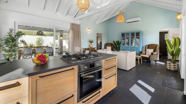 A modern kitchen with a central island, wooden cabinets, and a dining area with outdoor seating. - NEW Villa - Beautiful 3BR 2BA With Private Pool (Paradera)