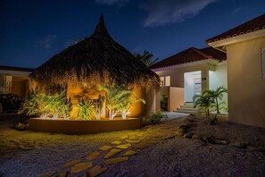 Relax in a serene outdoor space surrounded by tropical plants and a thatched-roof structure.