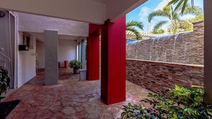A covered outdoor area with a stone floor, red pillars, and a stone wall with a water feature. - 2BR 1BA Ground Level in the Heart of Aruba Pool (Noord)