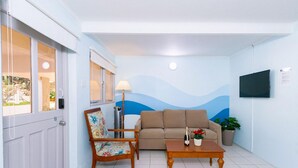 A living room with a sofa, a wooden coffee table, a floral armchair, a floor lamp, and a TV mounted on the wall. - 2BR 1BA Ground Level in the Heart of Aruba Pool (Noord)