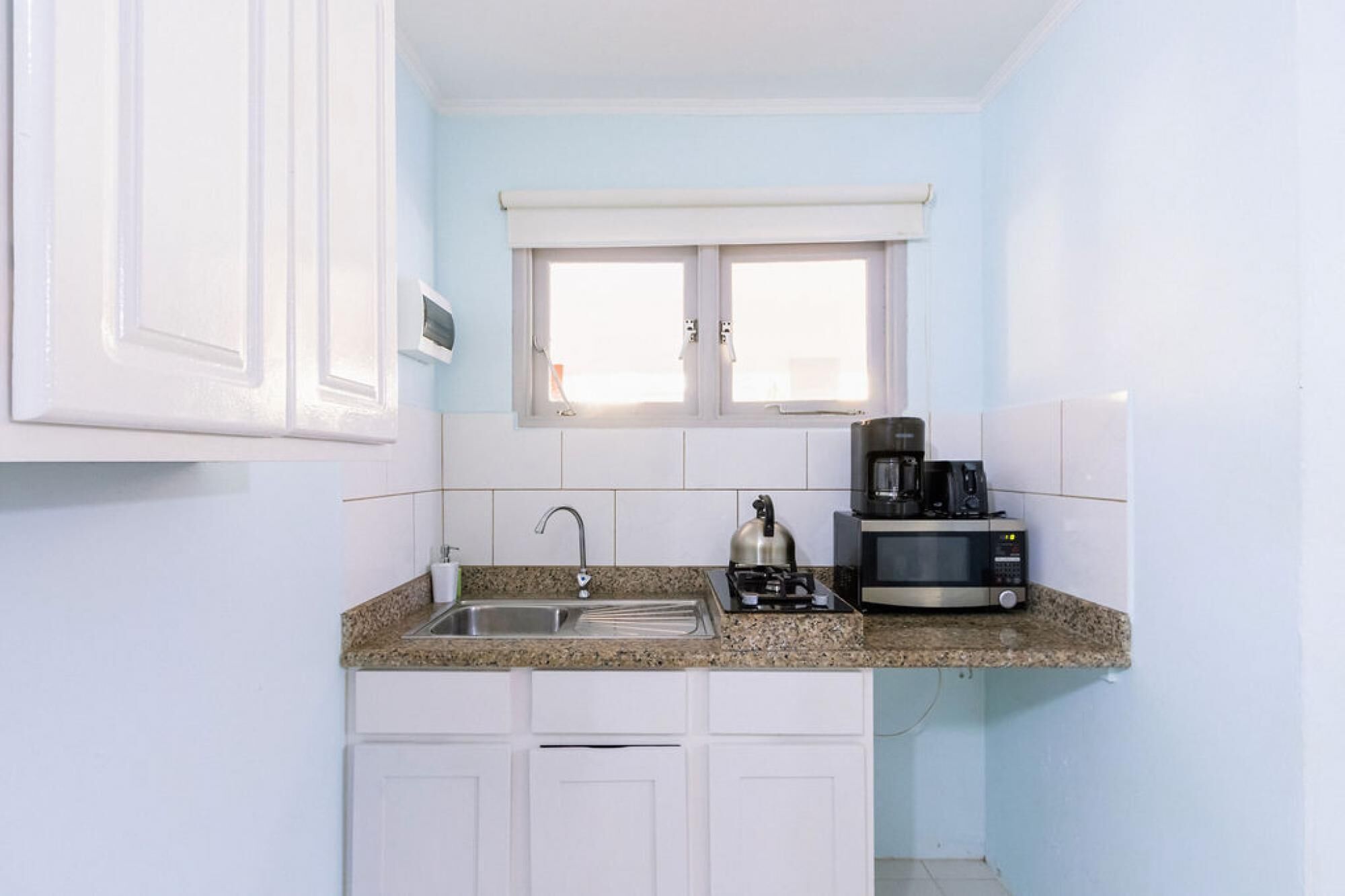 A compact kitchen with white cabinets, a granite countertop, a sink, a kettle, and a coffee maker.