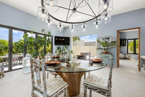 Enjoy meals in this stylish dining room with a large table and vintage-style chairs, surrounded by lush greenery views.