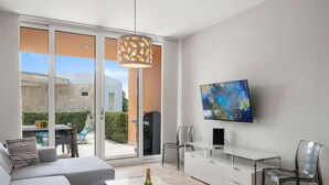 Een moderne woonkamer met een bank, salontafel, televisie en een schuifdeur naar een balkon.