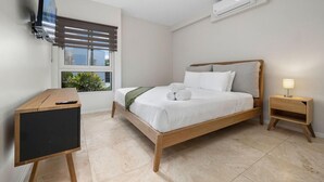 Een moderne slaapkamer met een houten bed, een bureau, een stoel, een aan de muur bevestigde televisie en een airconditioning.