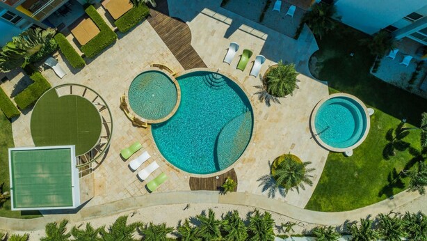 Luchtbeeld van een resort met meerdere zwembaden, ligbedden en palmbomen.