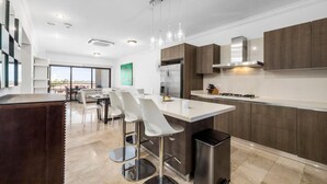 Une cuisine moderne dotée d’un îlot central, d’appareils électroménagers en acier inoxydable et d’un coin repas avec des chaises blanches.