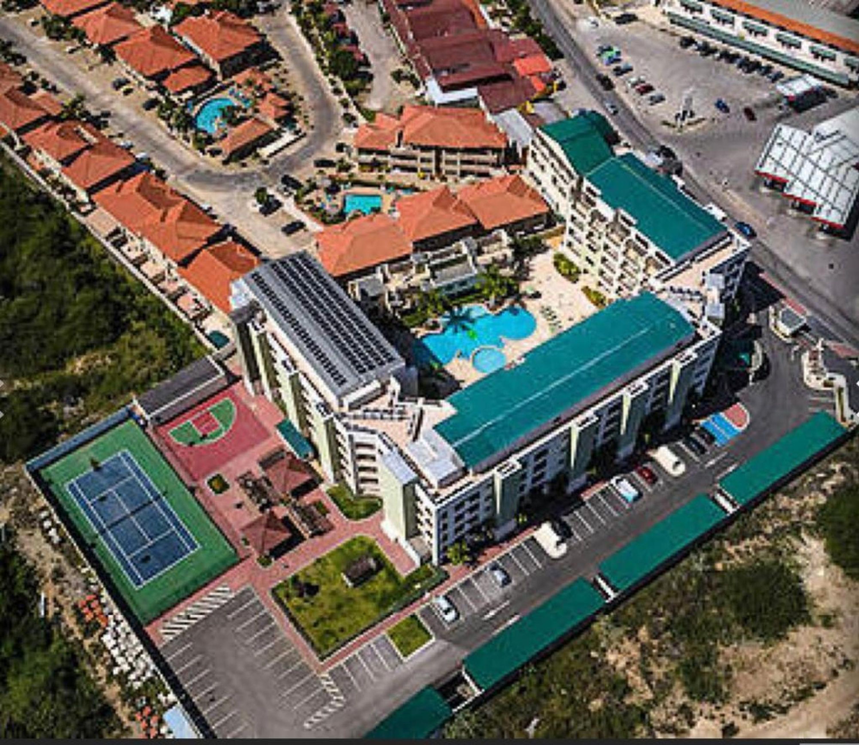 An aerial view of a hotel with multiple buildings, a swimming pool, and a tennis court.