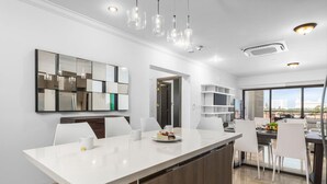 Une cuisine moderne dotée d’un grand îlot central, de meubles blancs et de luminaires suspendus.