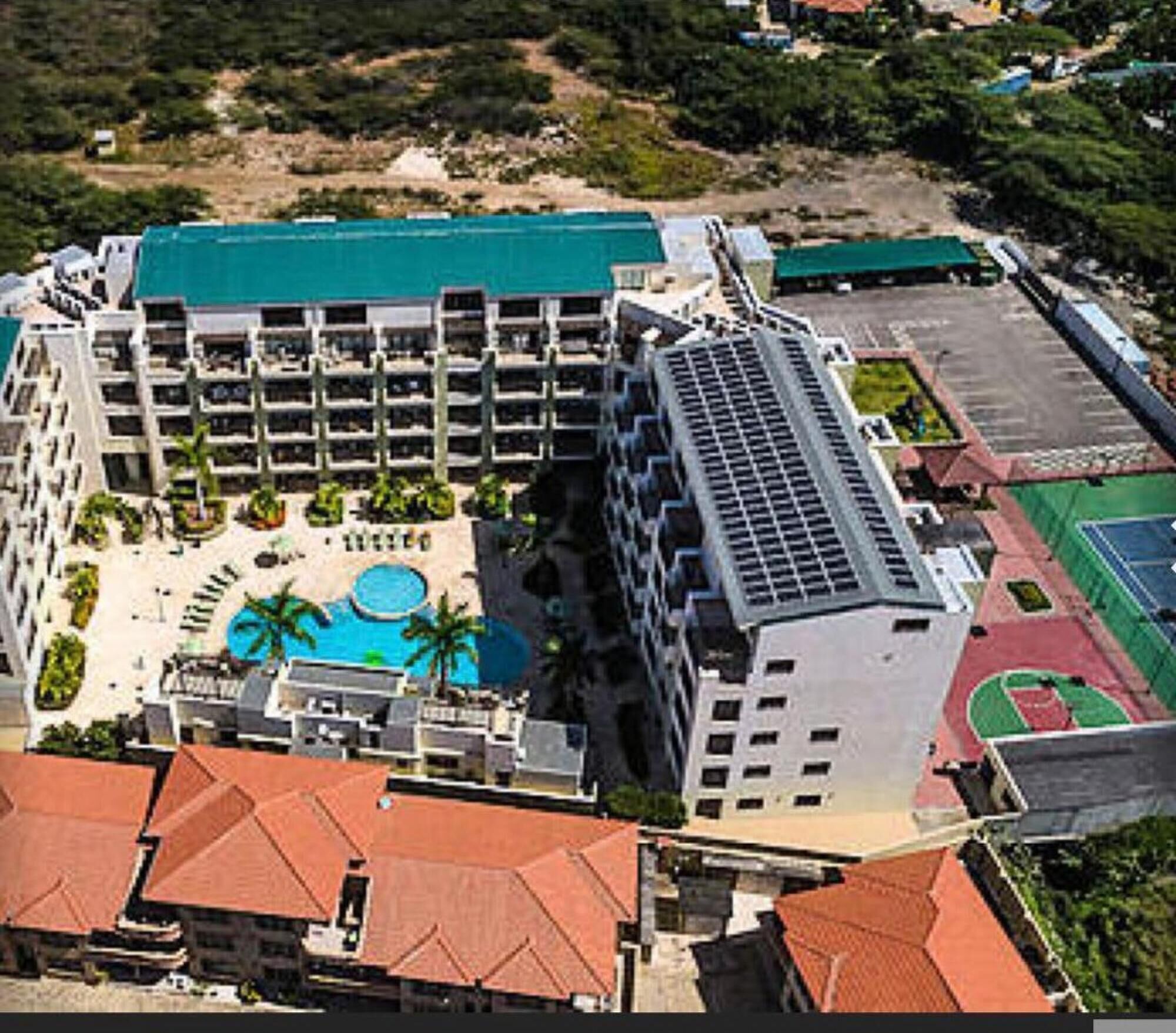 A large hotel with multiple floors, a central courtyard with a swimming pool, and a tennis court.