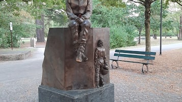 A statue of a seated figure on a pedestal in a park with a bench in the background.