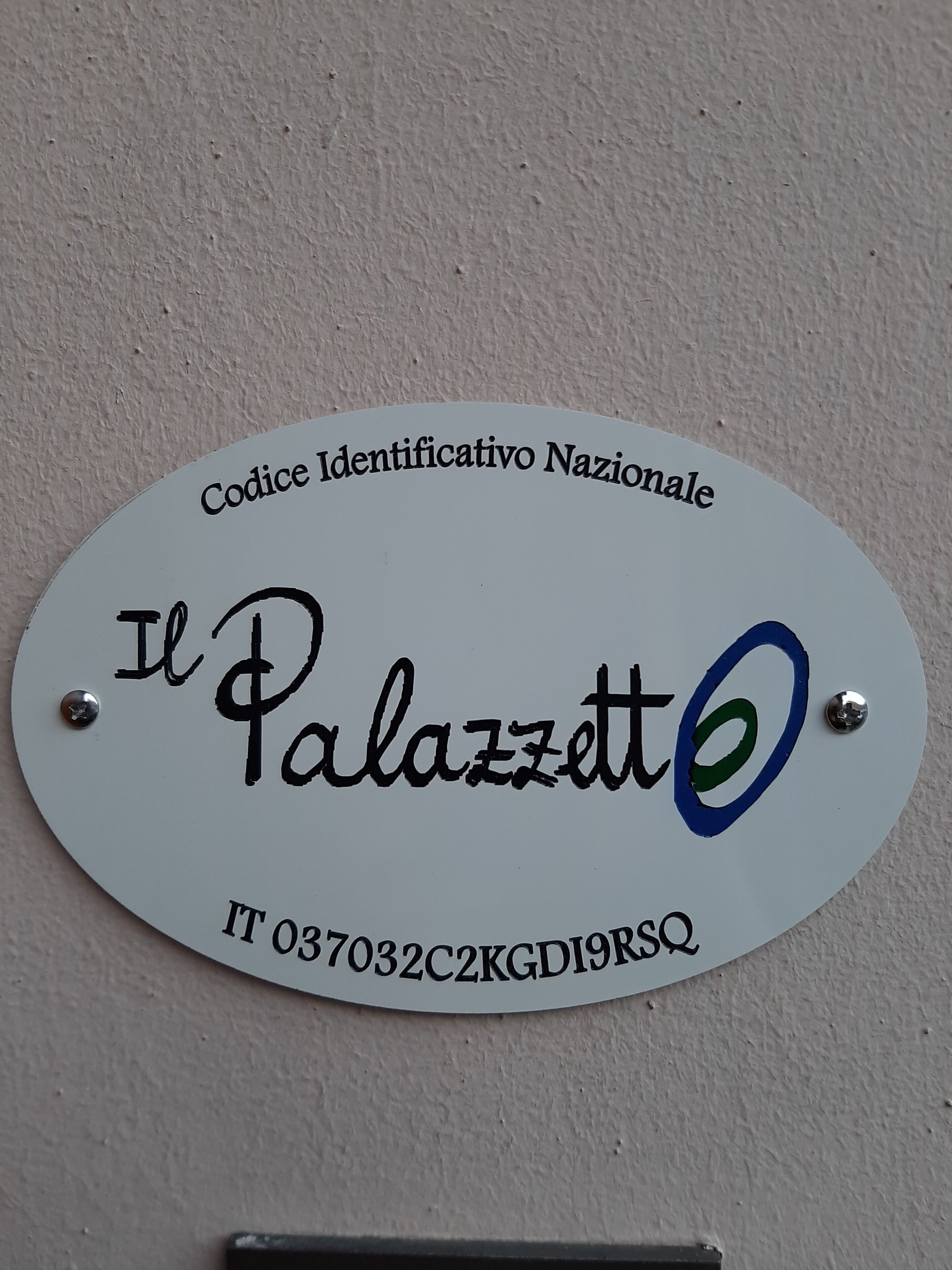 A white sign with black text and a blue circle. The text reads "Codice Identificativo Nazionale" at the top, "Il Palazzo" in the middle, and a code "IT 037032C2KGD19R5Q" at the bottom.