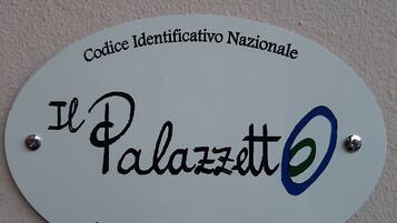 A white sign with black text and a blue circle. The text reads "Codice Identificativo Nazionale" at the top, "Il Palazzo" in the middle, and a code "IT 037032C2KGD19R5Q" at the bottom.