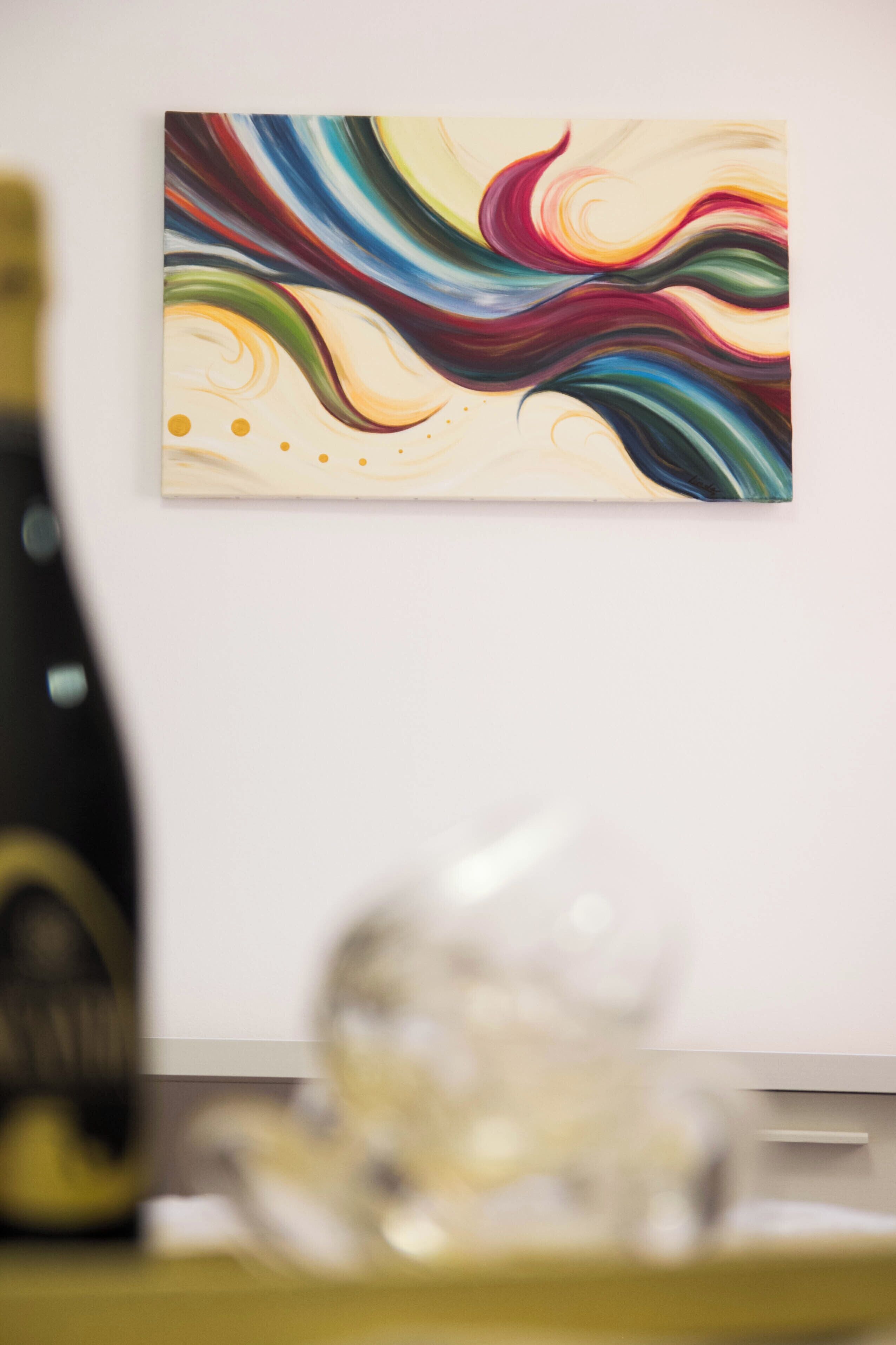 Une pièce avec un tableau abstrait accroché au mur, une bouteille de vin et un verre posés sur une table.