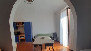 A dining area with a table and chairs, a kitchen area with cabinets and appliances, and a large window with curtains.