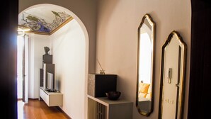 A hallway with an arched ceiling, a small shelf with a statue, a mirror, and a telephone on the wall.