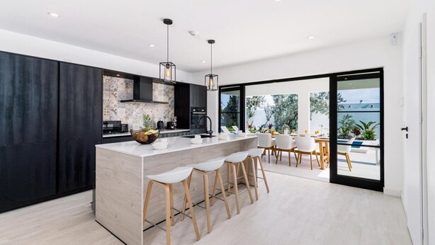 A modern kitchen with a central island, bar stools, and a dining area with a view. - Brand NEW 3br2ba Villa With Pool in Great Location (Noord)