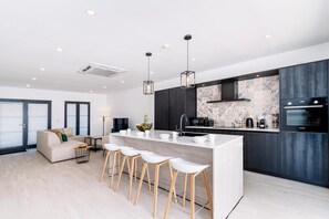 Une cuisine moderne dotée d’un îlot central, de tabourets de bar, d’un coin repas avec un canapé et d’une grande fenêtre.