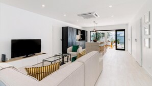 A modern living room with a sofa, a TV, and a dining area with a table and chairs. - Brand NEW 3br2ba Villa With Pool in Great Location (Noord)