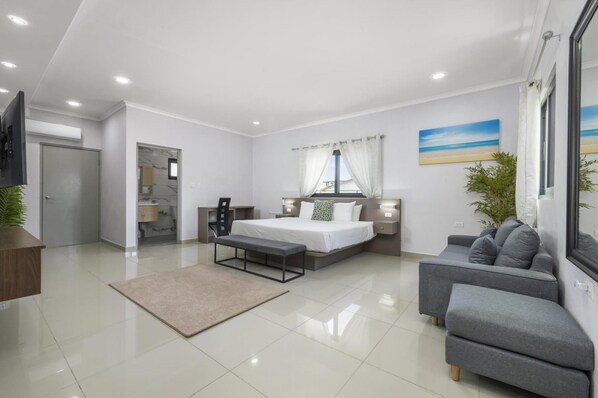 A modern bedroom with a bed, a sofa, a desk, and a bathroom visible through an open door. - NEW 4br4ba Villa Across of Palmbeach w Pvt Pool (Noord)