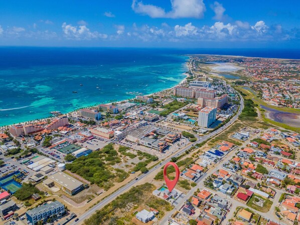 An aerial view of a coastal city with a mix of residential and commercial buildings, a prominent hotel, and a clear view of the ocean.