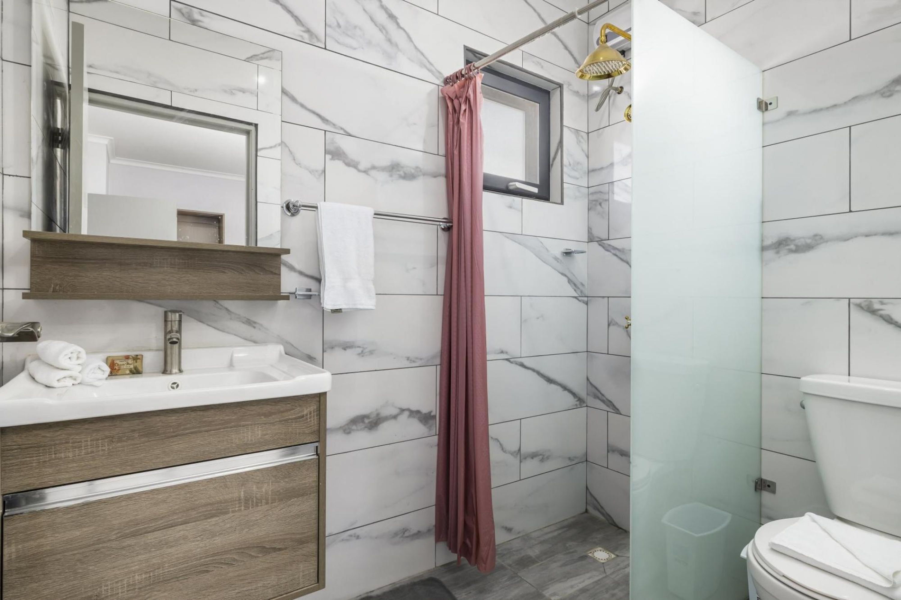 Une salle de bain avec un mur recouvert de carreaux de marbre, un meuble-lavabo en bois avec un évier, un miroir et un rideau de douche.