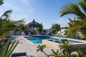 Uma área de piscina com espreguiçadeiras e um guarda-sol de palha.