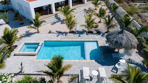 Uma área de piscina com uma piscina retangular, espreguiçadeiras e palmeiras.