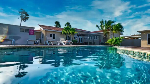 A swimming pool with lounge chairs and palm trees, surrounded by buildings with a tiled roof. - Spacious 6BR Villa w Pool Close2beach Sleeps 16 (Noord)