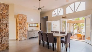 A spacious dining area with a stone accent wall, a ceiling fan, and a view of the outdoor patio. - Spacious 6BR Villa w Pool Close2beach Sleeps 16 (Noord)