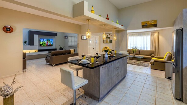 A modern kitchen with a central island, a dining area with a sofa, and a living room with a TV. - Sleeps 16 Palm Beach - 6BR Villa w Private Pool (Noord)