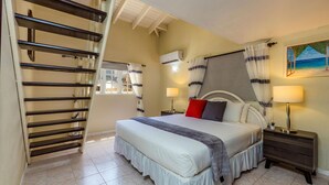 A bedroom with a bed, a nightstand, a lamp, a painting, a window with curtains, and a staircase. - Sleeps 16 Palm Beach - 6BR Villa w Private Pool (Noord)