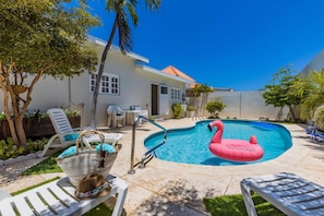 A swimming pool with a pink flamingo float, surrounded by white lounge chairs and a wicker basket. - Sleeps 16 Palm Beach - 6BR Villa w Private Pool (Noord)