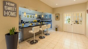 A modern kitchen with a central island, bar stools, pendant lighting, and a 'HOME SWEET HOME' sign. - Sleeps 16 Palm Beach - 6BR Villa w Private Pool (Noord)