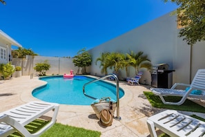 Patio con piscina, sillas de descanso, una parrilla y palmeras.