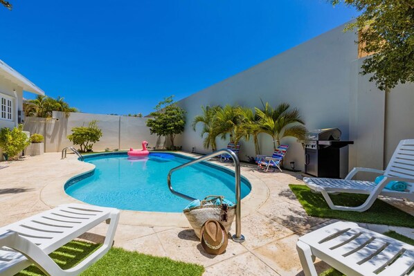 A backyard with a swimming pool, lounge chairs, a grill, and palm trees. - Sleeps 16 Palm Beach - 6BR Villa w Private Pool (Noord)
