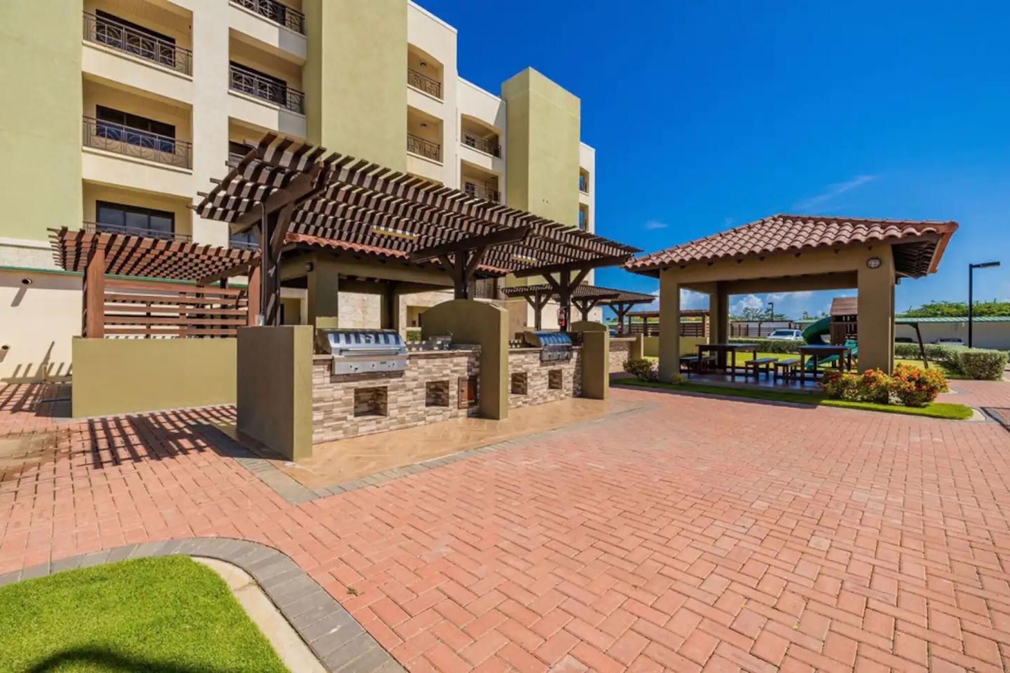 Un patio con una parrilla, mobiliario exterior y un edificio al fondo.