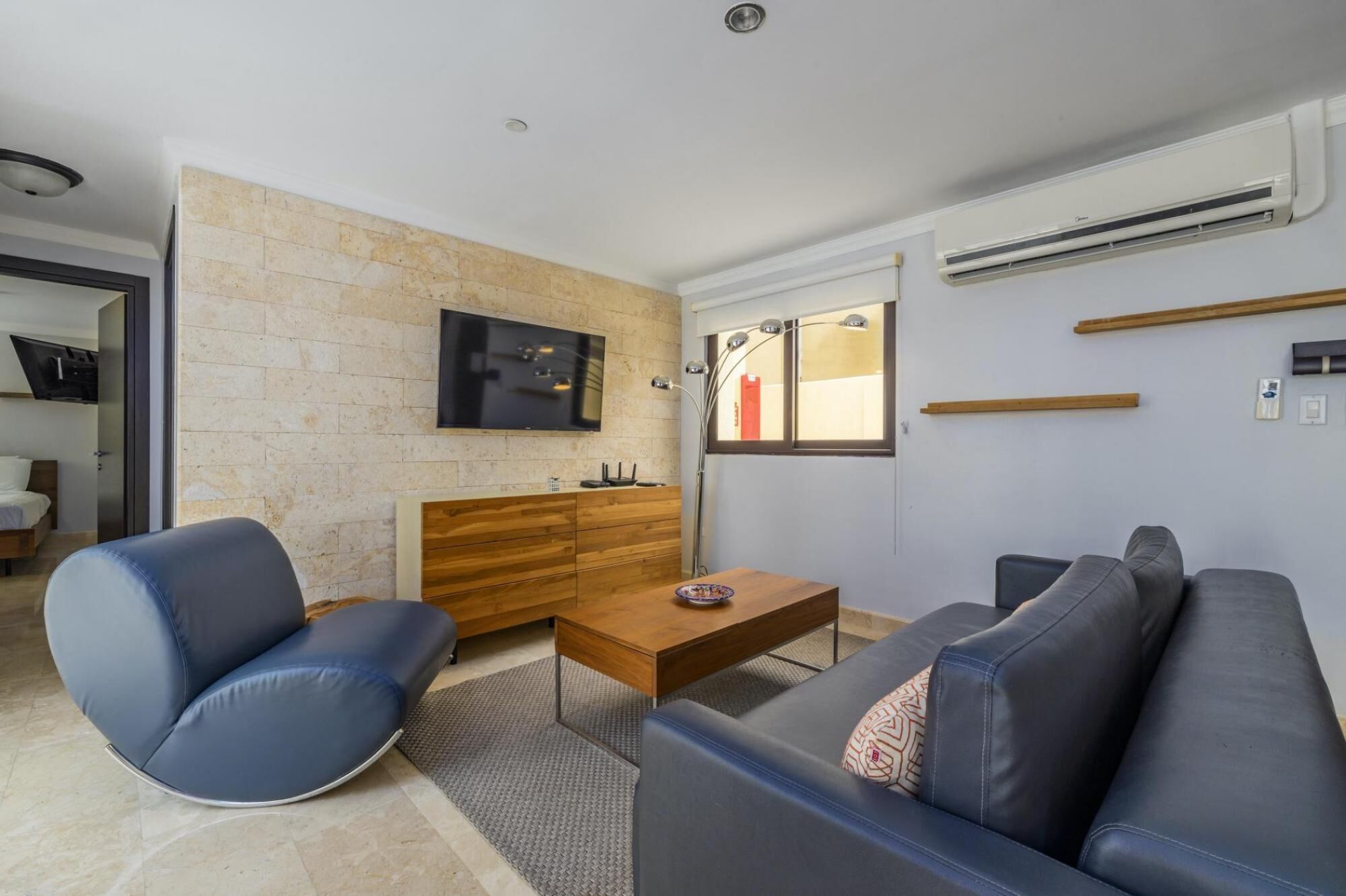 Una sala moderna con pared de piedra, televisor de pantalla plana, mesa de centro de madera, sofá y escritorio.