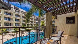 Uma varanda com vista para uma piscina, área de estar externa e um edifício com várias varandas.