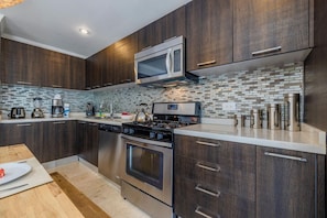 Kitchen features stainless steel appliances, a sink, and a stove on a small island, with a backsplash of gray and white tiles.