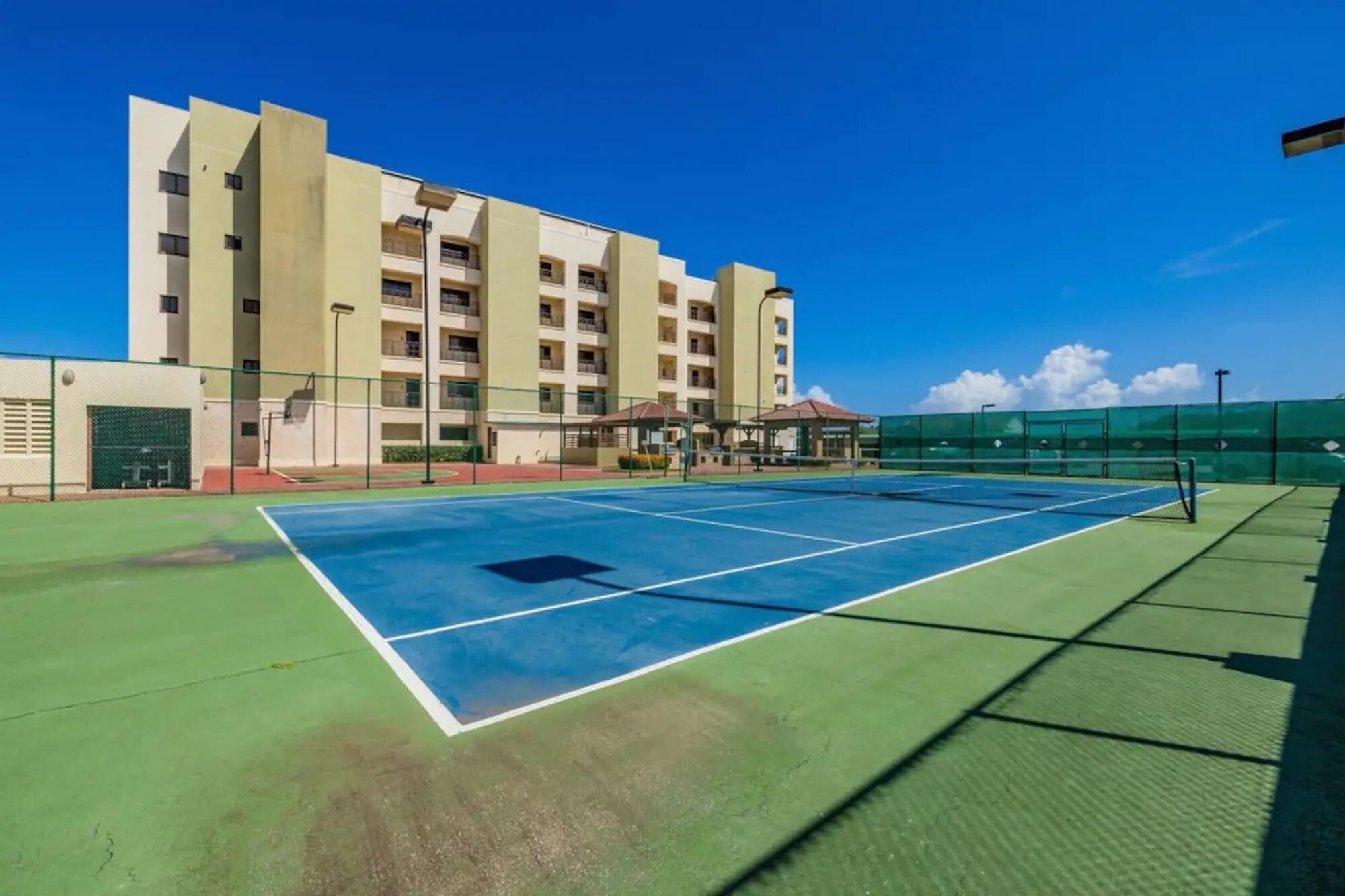 An outdoor tennis court with a building in the background.