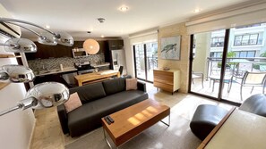 Relax in this spacious living area with a sofa and coffee table, offering a view of the outdoor balcony through large windows.