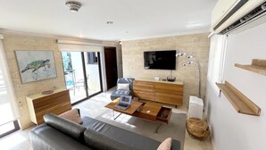 Uma sala de estar moderna com sofá, mesa de centro, TV e uma porta de vidro deslizante que dá para uma varanda.